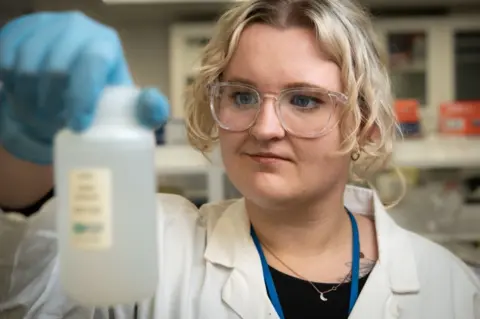 Tony Jolliffe/BBC Phd researcher Laura Taylor holds a small bottle of water containing melted water from the iceberg