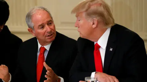 Reuters/Kevin Lamarque Stephen Schwarzman gestures with his hands as he speaks to US president Donald Trump who is sat beside him to his left at a meeting at the White House in 2017. Both men are wearing dark suits with light shirts and vibrant red ties. 