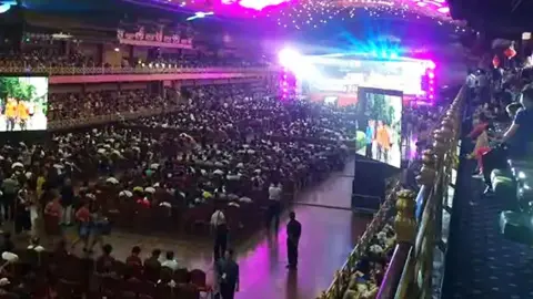 Chinese social media Hundreds of people are seated in a huge venue in China - there is a stage at the far end of the hall and two big screens showing video. There is purple and blue neon lighting over the event.