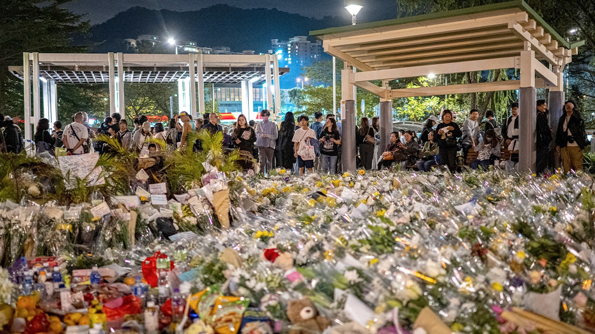 Mourners gather outside a Hong Kong housing complex to place flowers in remembrance of fire victims.